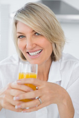 Happy woman having orange juice in kitchen