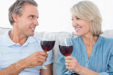 Couple toasting each other with red wine on the sofa