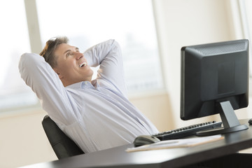 Happy Businessman With Hands Behind Head Sitting At Desk