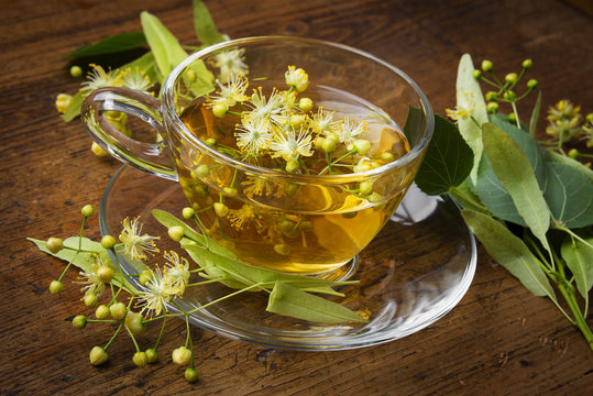 a cup with linden tea and flowers on wooden table