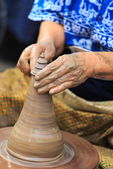 Potter hands making in clay on pottery wheel.