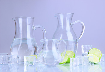 Glass pitchers of water with ice and lime on grey background