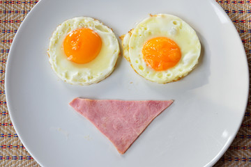 breakfast smiley face with bacon and fried eggs on white plate