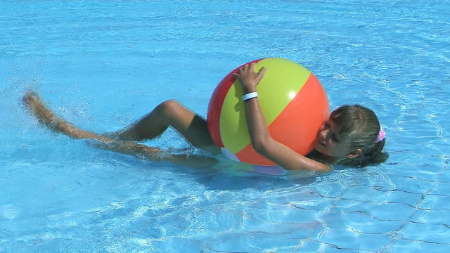 Child playing with beach ball in swimming pool.