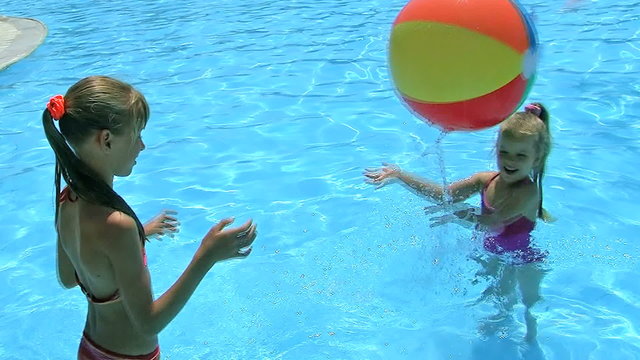 Children playing beach ball in swimming pool.