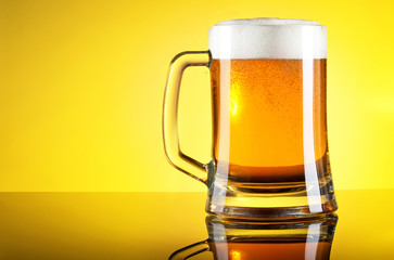 Glass of beer close-up with froth over yellow background