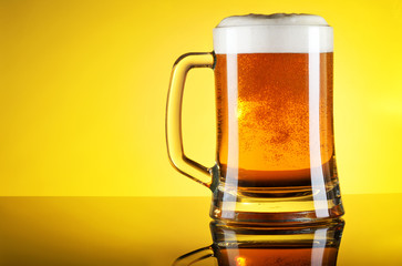 Glass of beer close-up with froth over yellow background