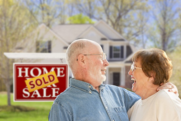 Senior Couple in Front of Sold Real Estate Sign and House