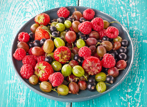 Plate of fresh ripe berries on blue wooden background