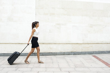 Young Woman Walking with Luggage on Wall Background.
