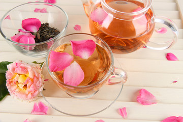 Kettle and cup of tea from tea rose on wooden background