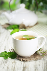Teapot and cup of herbal tea with fresh mint on wooden table