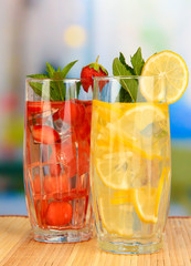 Glasses of fruit drinks with ice cubes on table in cafe
