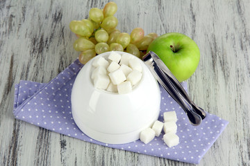 Refined sugar in white sugar bowl on wooden background