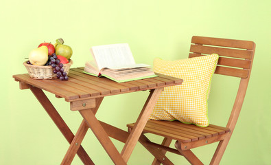 Wooden table with fruit and book on it on green background