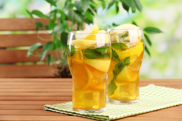 Iced tea with lemon and mint on wooden table, outdoors