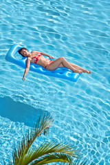 Woman in red swimsuit bakes on inflatable mattress in pool