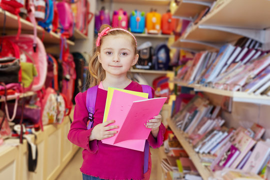 Little girl stands in school department of store with backpack