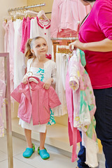Little girl stands holding hanger with pink jacket