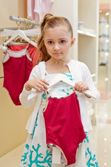 Little girl stands holding hanger with closed swimsuit