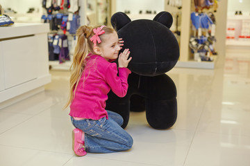 Little girl sits squatted and sqeezing up to big stuffed toy
