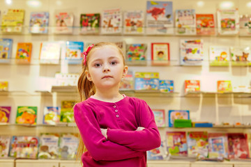 Little girl stands with arms folded on chest in book department