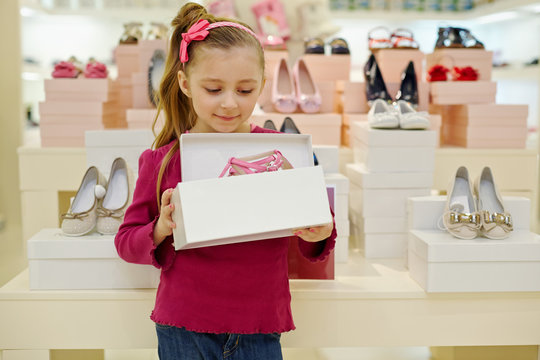 Little girl stands and holds open box with pink shoes