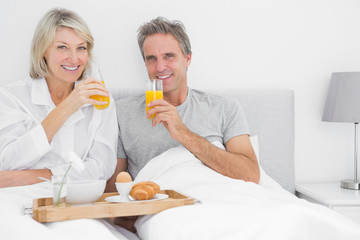 Obraz na płótnie Canvas Couple drinking orange juice at breakfast in bed