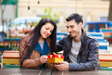 The young man gives a gift to a young girl in the cafe