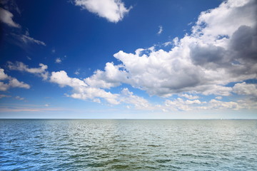 Naklejka na ściany i meble Cloudy blue sky above a surface of the sea