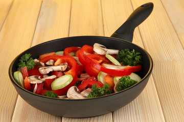frying pan with vegetables on wooden background