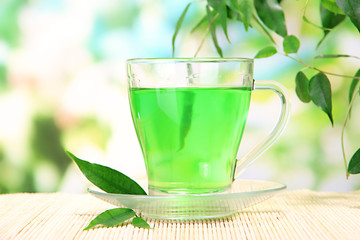 Transparent cup of green tea on bamboo mat, on nature