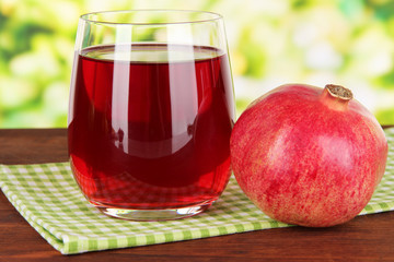 Glass of fresh garnet juice on table on bright background