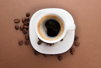 Cup of coffee with coffee beans on brown background