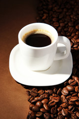 Cup of coffee with coffee beans on brown background