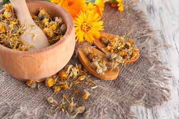 Fresh and dried calendula flowers in mortar on wooden