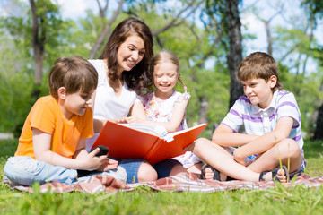 Fototapeta premium teacher reads a book to children in a summer park