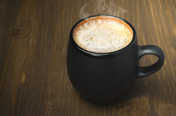 black mug of coffee with froth and space for text