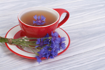Fototapeta na wymiar Tea with petals of wild cornflowers in a red cup on the table