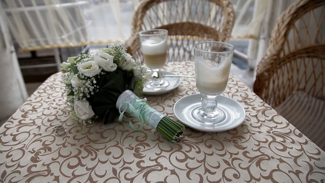 Two cups with cappuchino with wedding bouquet on the table