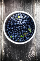 Blueberries in a bowl with leaves on wooden old rustic  backgrou
