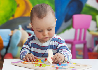 Naklejka premium Toddler or a baby child playing with puzzle in a nursery.