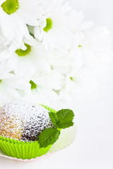 Muffin mit Minzblatt und Blumen im Hintergrund