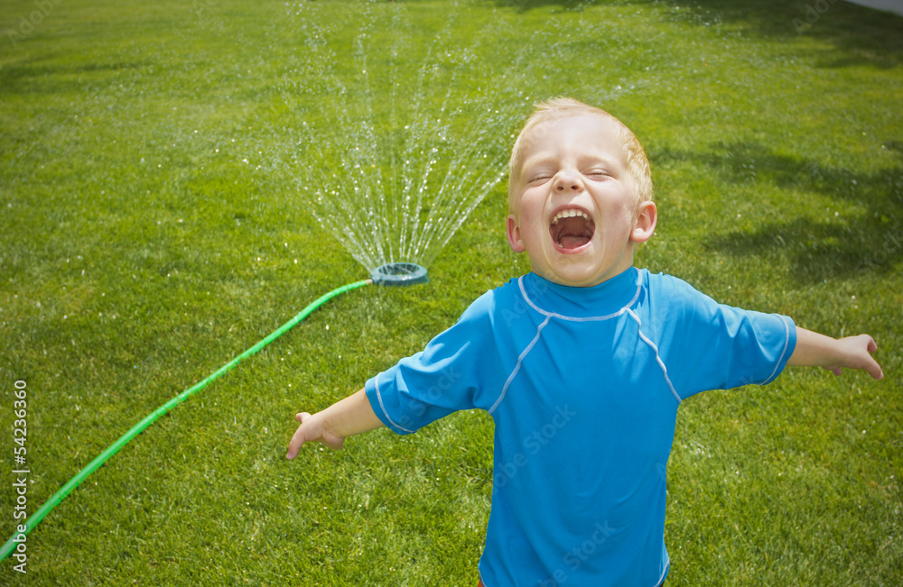 Wall mural Young boy playing in the sprinklers outdoors