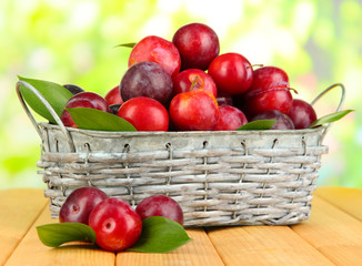 Ripe plums in basket on wooden table on natural background