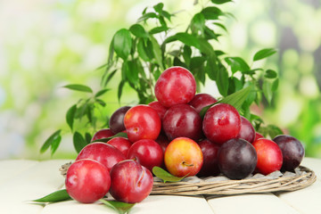 Ripe plums in basket on wooden table on natural background