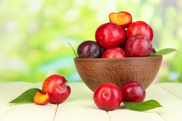 Ripe plums in bowl on wooden table on natural background