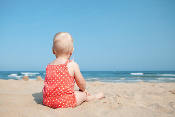 Little girl sitting on sand at beach