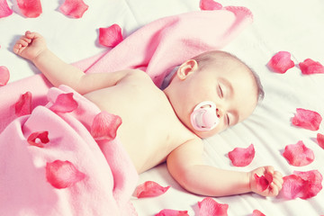 Fototapeta na wymiar Toddler girl sleeping in a bed strewn with rose petals in. In th