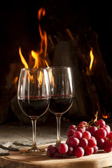 Copas de vino uvas y fuego en chimenea de fondo.